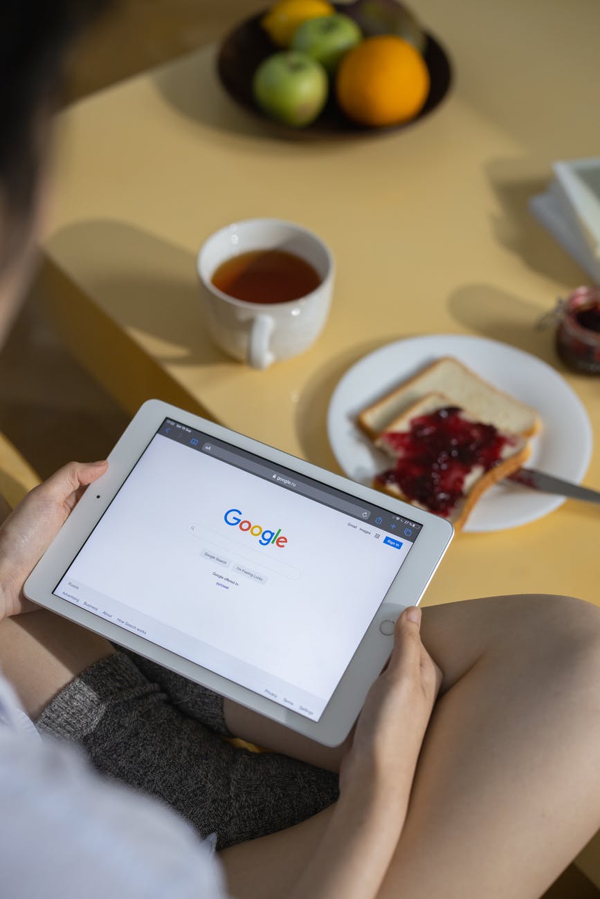 person holding white ipad near white ceramic mug with coffee